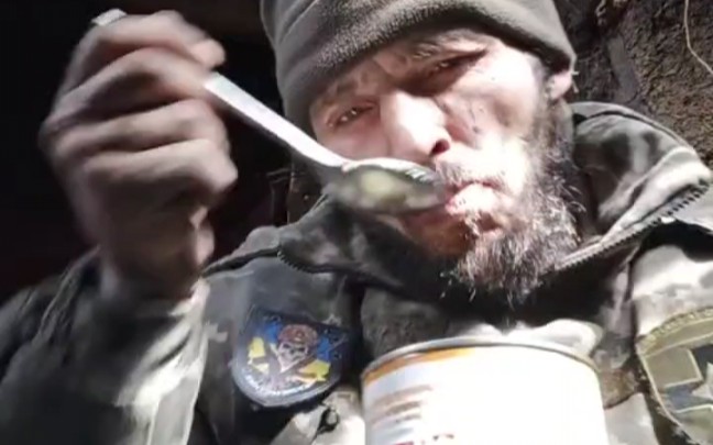 俄乌战争前线掩体内，一名乌军士兵正在进餐，简单的豆子罐头配面包、香肠。