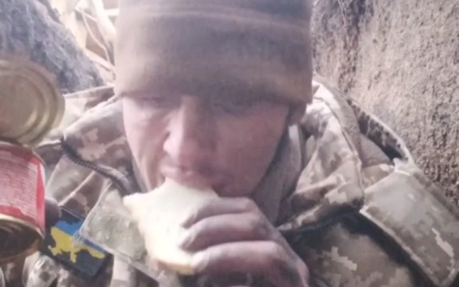 俄乌战争的冬季前线战壕中，一名乌军士兵在吃午餐，简单的冷鱼罐头配面包。