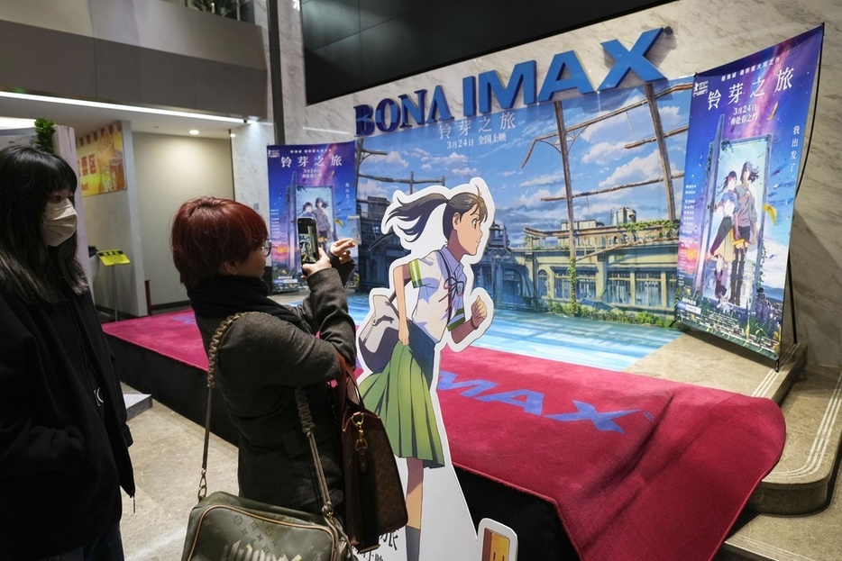 映画館内に設けられたアニメ映画「すずめの戸締まり」の看板の前で写真を撮る人たち＝3月、北京